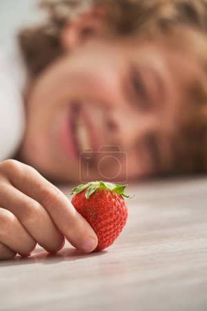 Photo for Closeup of hand of smiling child resting head on floor and looking at sweet berry at home on weekend day - Royalty Free Image