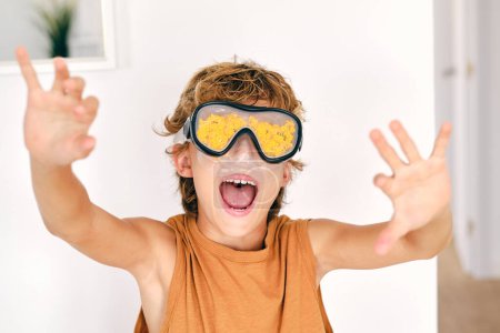 Téléchargez les photos : Enfant excité dans des lunettes de plongée avec des cris d'algues avec les bras tendus dans la pièce de la maison lumière - en image libre de droit