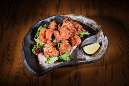 Photo for From above of crunchy deep fried chicken wings on pile of salad leaves served on plate with wedge of lime - Royalty Free Image