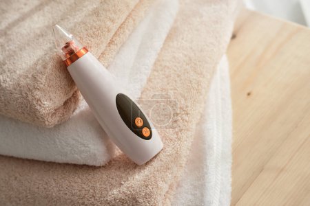 Photo for High angle of blackhead vacuum cleaner placed on pile of towels on wooden table in light room at home - Royalty Free Image