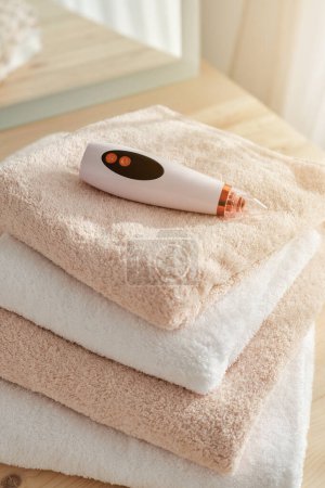 Photo for From above of electric blackhead vacuum remover placed on heap of soft towels on table in light room at home - Royalty Free Image