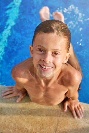Photo for Top view of happy boy with wet hair smiling and looking at camera while swimming in pool during summer vacation at resort - Royalty Free Image