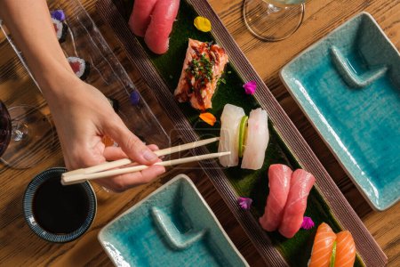 Foto de Vista superior de la cosecha persona anónima comiendo sushi nigiri con palillos de bambú en la cena gourmet japonesa - Imagen libre de derechos