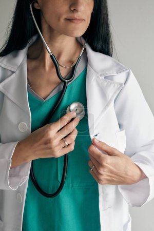 Foto de Médico femenino anónimo en uniforme médico escuchando ritmo cardíaco con estetoscopio profesional sobre fondo claro - Imagen libre de derechos