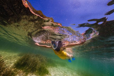 Photo for From below of anonymous diver in snorkeling mask swimming in calm transparent ocean water during summer vacation - Royalty Free Image