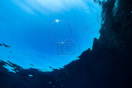 Téléchargez les photos : Par le dessous de l'anneau à bulles sous-marin flottant dans un océan clair contre un ciel bleu sans nuages par une journée ensoleillée - en image libre de droit