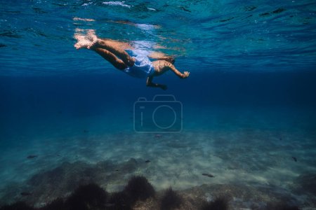Foto de Vista posterior de longitud completa de niño anónimo en máscara de snorkel y pantalones cortos nadando bajo el agua azul claro y explorando el fondo del mar - Imagen libre de derechos
