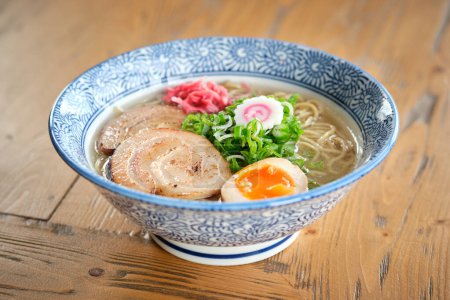 Photo for From above of fresh cooked ramen soup with pork and noodles served in white ceramic plate with blue ornament on wooden table - Royalty Free Image