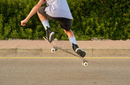 Foto de Vista posterior de la cosecha irreconocible skater preadolescente en el momento de saltar con monopatín sobre la carretera en la puesta del sol - Imagen libre de derechos