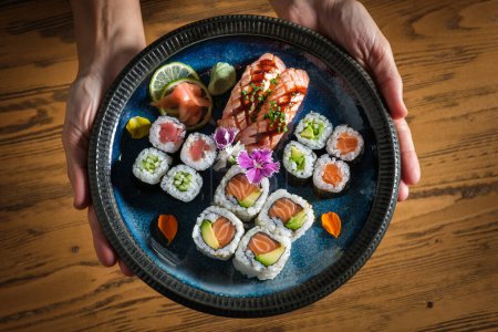 Téléchargez les photos : Vue du dessus de la récolte personne anonyme tenant assiette avec assortiment savoureux rouleaux de sushi japonais avec du poisson cru et du gingembre avec wasabi sur des tranches de citron vert - en image libre de droit