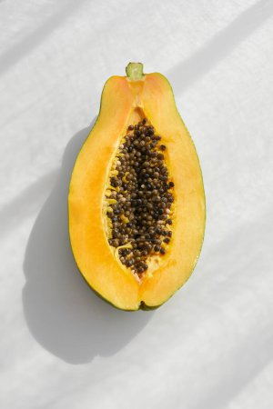 Photo for Overhead view of halved exotic ripe papaya fruit with seeds placed on table in bright sunlight with shadow in studio - Royalty Free Image