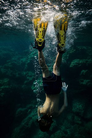 Foto de Vista posterior cuerpo completo de buzo masculino anónimo en traje de neopreno y aletas buceando bajo agua de mar transparente con arrecifes de coral en el fondo - Imagen libre de derechos