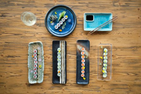Foto de Vista superior de surtidos de sushi y rollos en diferentes platos de mármol colocados en mesa de madera con palillos y copa de vino - Imagen libre de derechos