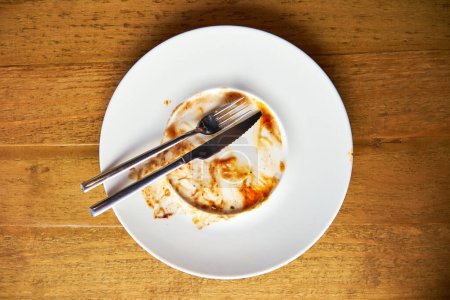 Foto de Foto aérea de tenedores dispuestos en un plato de cerámica blanca con residuos de salsa en una superficie de madera - Imagen libre de derechos