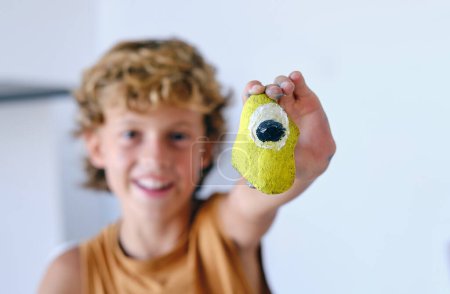 Téléchargez les photos : Floue créatif préadolescent garçon tendre la main et montrant lumineux peint rocher à caméra - en image libre de droit