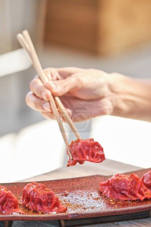 Foto de Cultivo persona anónima con palillos de madera comiendo aperitivos jiaozi con especias de plato de cerámica servido en la mesa - Imagen libre de derechos