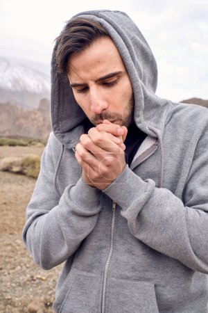 Photo for Focused unshaven Hispanic male traveler warming hands while waling against mountain Teide and looking down in Tenerife Canary Islands Spain - Royalty Free Image