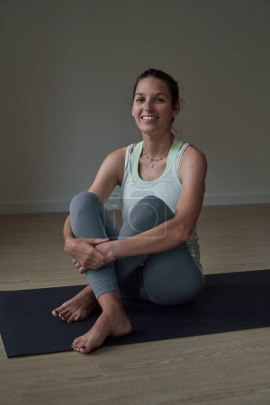Photo for Full body of young fit female in sportswear sitting on mat and looking at camera while practicing yoga at gym - Royalty Free Image