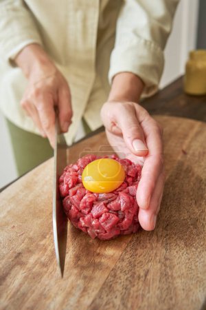 Photo for From above of unrecognizable chef making round shape of raw beef with egg yolk on cutting board in kitchen while cooking steak tartare - Royalty Free Image