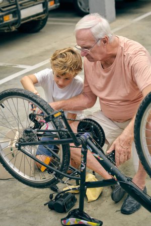 Corps complet de grand-père sérieux gonflant des pneus de vélo près du petit-fils regardant la roue avec attention
