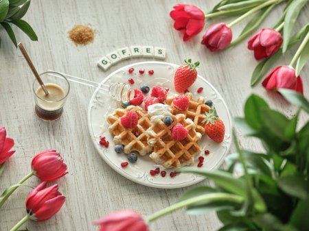 Photo for From above of sweet homemade waffles topped with berries served near Gofres scrabble inscription on table with coffee and tulips - Royalty Free Image