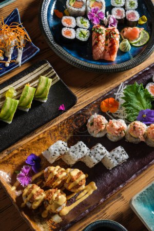 Téléchargez les photos : D'en haut de savoureux rouleaux de sushi frais avec diverses garnitures servies sur des plateaux avec des fleurs décoratives sur une table en bois dans un café - en image libre de droit