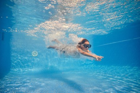 Téléchargez les photos : Corps complet de garçon en lunettes de natation dans les bulles d'eau dans la piscine pour passe-temps - en image libre de droit