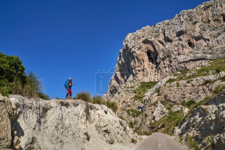 Téléchargez les photos : Vue latérale du randonneur masculin debout sur le bord d'une falaise rocheuse et observant les montagnes dans la nature pendant les vacances d'été - en image libre de droit