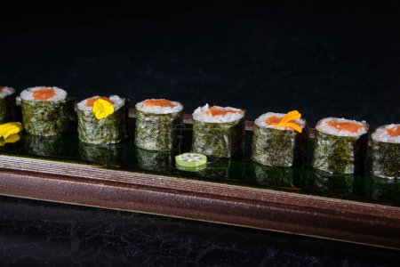 Foto de Deliciosos rollos de sushi con salmón servidos en bandeja de madera colocados sobre mesa de mármol en restaurante sobre fondo borroso - Imagen libre de derechos