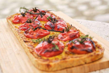 Photo for Rectangular shaped flatbread with tomato slices and thyme sprigs on wooden chopping board on blurred background - Royalty Free Image