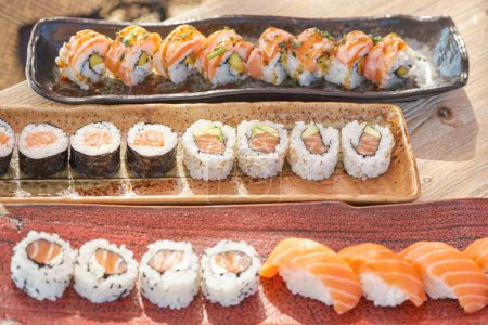 Photo for From above of appetizing sushi set consisting of Philadelphia and California rolls tekkamaki and sake nigiri served on ceramic trays placed in row on wooden table - Royalty Free Image