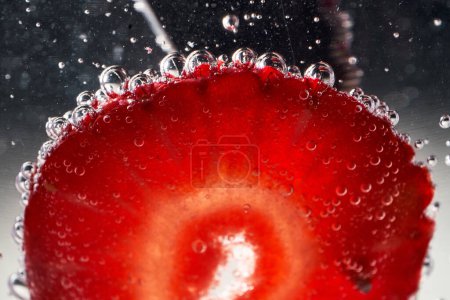 Téléchargez les photos : Gros morceau de fraise rouge mûre placé à l'intérieur du verre de boisson gazeuse avec des bulles transparentes - en image libre de droit