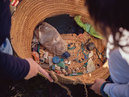 Téléchargez les photos : D'en haut de la récolte enfants préadolescents méconnaissables observant tas de déchets en plastique ramassés et les ordures sur le fond du sac en osier - en image libre de droit