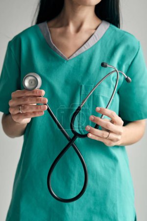 Photo for Crop anonymous female doctor in green medical uniform with stethoscope at work in daytime - Royalty Free Image