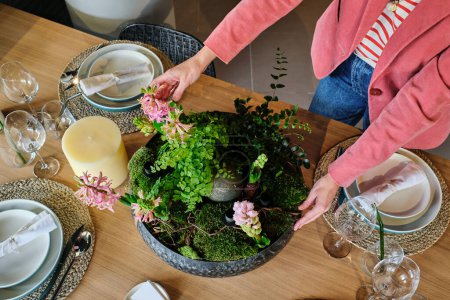 Photo for From above of unrecognizable housewife placing ceramic flowerpot with planted hyacinths on table while serving table for lunch in modern kitchen at home - Royalty Free Image