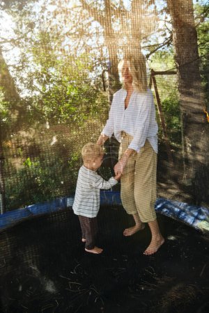 Photo for Full body of woman and son in casual clothes jumping on edge of trampoline in playground - Royalty Free Image