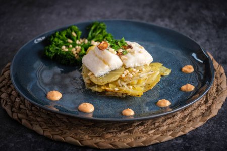 Téléchargez les photos : Grand angle de gratin exquis au poisson blanc avec sauce et brocoli aux pignons de pin sur une assiette placée sur un support en osier - en image libre de droit