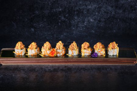 Photo for Appetizing sushi topped with salmon and fresh sauce served with flowers on wooden tray placed on table in restaurant against black background - Royalty Free Image