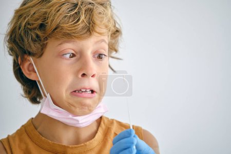 Téléchargez les photos : Enfant effrayé regardant écouvillonnage en main d'un médecin anonyme pendant l'examen COVID 19 à l'hôpital sur fond de lumière - en image libre de droit