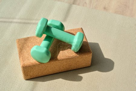 Photo for From above of light green dumbbells placed on yoga block on mat in sunlight - Royalty Free Image