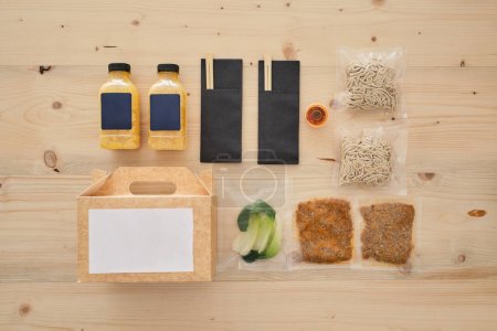 Foto de Vista superior de la composición de los ingredientes, incluyendo caldo de fideos y carne con hojas de col china en bolsas de vacío cerca de la caja y palillos - Imagen libre de derechos