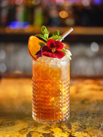 Téléchargez les photos : Cocktail long avec glaçons décorés de fleurs et de tranches d'orange séchées servi dans un bar moderne sur fond flou - en image libre de droit