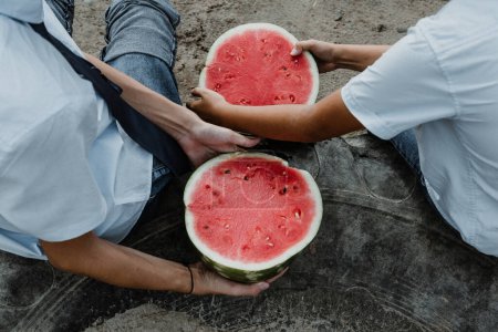 Photo for From above of crop anonymous male students in uniform sitting by floor and eating delicious freshly sliced watermelon in daylight - Royalty Free Image