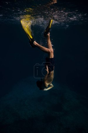 Téléchargez les photos : Vue latérale complète du corps du plongeur masculin anonyme en masque de plongée et palmes nageant sous l'eau profonde de la mer sombre - en image libre de droit