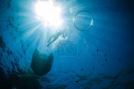 Photo for From below underwater view of anonymous kid in mask snorkeling in deep sea near catamaran and ring bubble on surface under vibrant sun rays - Royalty Free Image