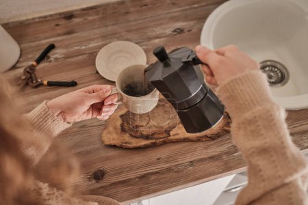 Téléchargez les photos : De dessus de la récolte femelle anonyme dans un pull chaud versant du café chaud de la cafetière geyser dans une tasse dans la cuisine - en image libre de droit