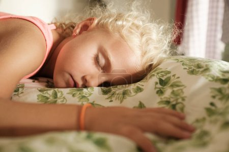 Téléchargez les photos : Vue latérale d'adorable fille blonde dormant sur un lit confortable dans la chambre à coucher à la maison - en image libre de droit