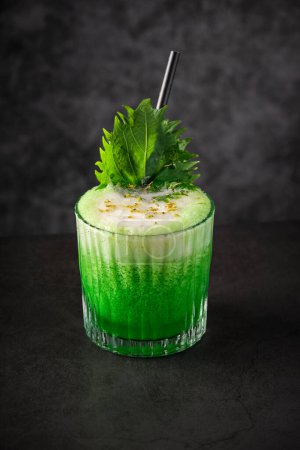 Photo for From above of glass filled with refreshing green alcohol cocktail decorated with froth shiso leaf and grated camomile flower served in restaurant - Royalty Free Image