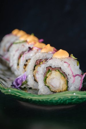 Foto de Fila de apetitosos rollos de uramaki servidos en bandeja de mármol con salsa y flores en la cafetería sobre fondo borroso - Imagen libre de derechos