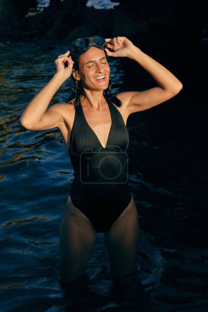 Téléchargez les photos : Touriste souriante aux yeux fermés en maillots de bain et lunettes de plongée profitant de la lumière du soleil dans la mer ondulée - en image libre de droit